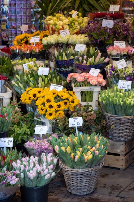 A vibrant display of fresh floral bouquets and individual flower bunches arranged in various containers at a flower shop. The scene showcases a variety of colorful flowers, including yellow sunflowers