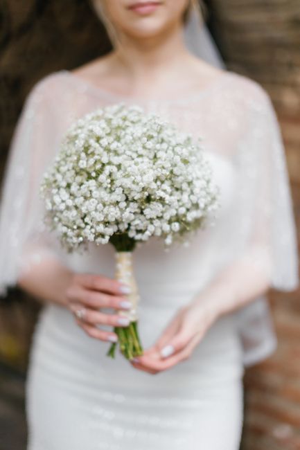 A bride holding a round bouquet of delicate white baby's breath flowers, wrapped with a cream satin ribbon. The bouquet is generously sized, with tiny, soft petals creating a cloud-like appearance. Sh