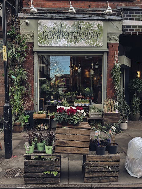 The exterior of Northern Flower, a flower shop with a vintage-style sign featuring green lettering and decorative foliage. The shop has a large front window displaying various plants and floral arrang